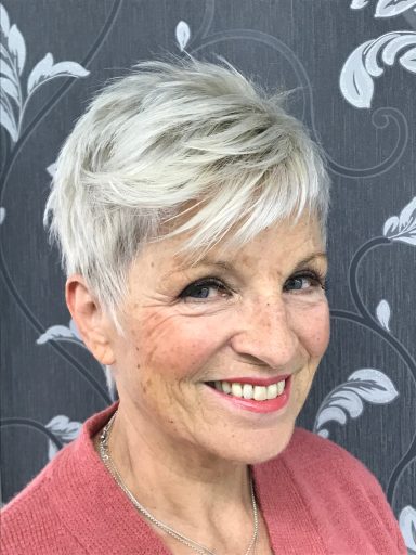 Eine hellblonde Frau mit einer pfiffigen Kurzhaarfrisur lächelt.