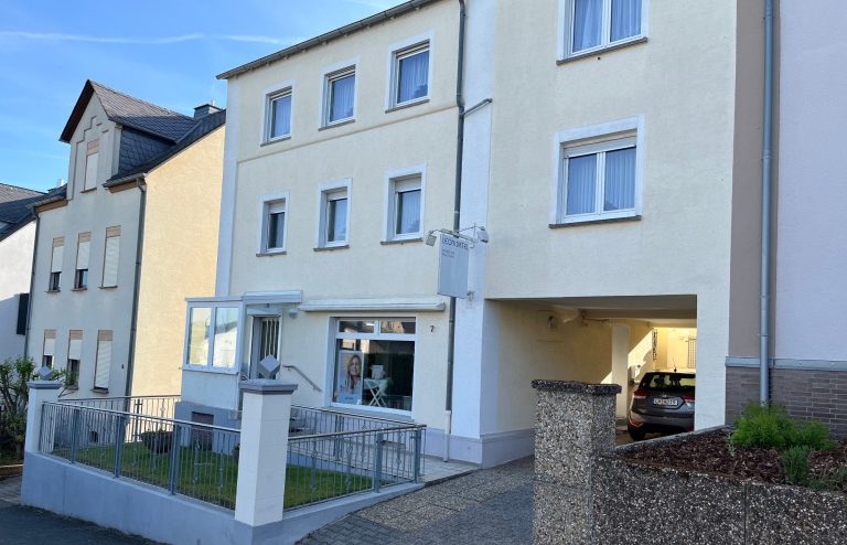 Ein gelbes Mehrfamilienhaus mit Schild "Leoni Distel Frisuren und Nagelstudio"